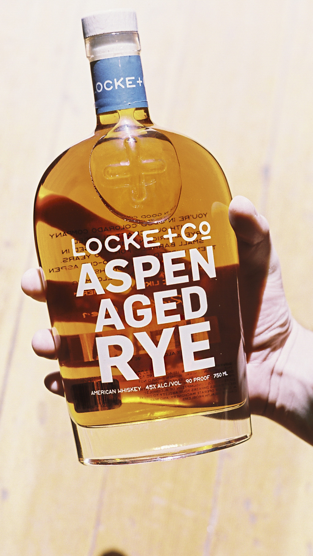 A hand holding a Locke + Co. Aspen Aged Rye Whiskey Bottle