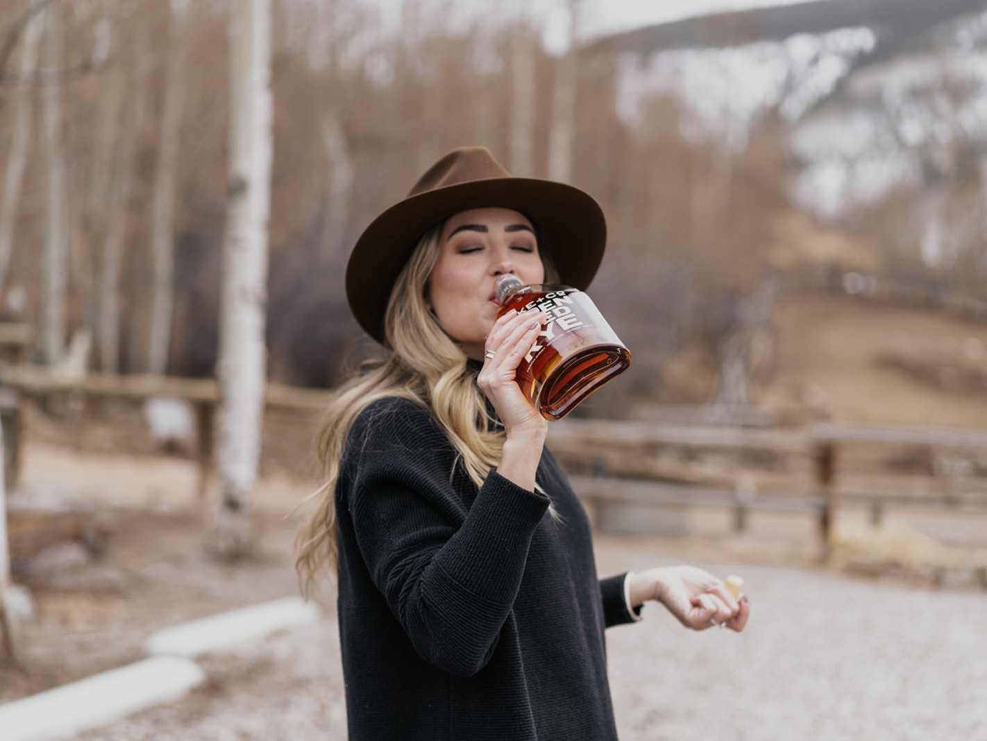 Women in a hat drinking Locke + Co Aspen Aged Rye Whiskey straight from the bottle