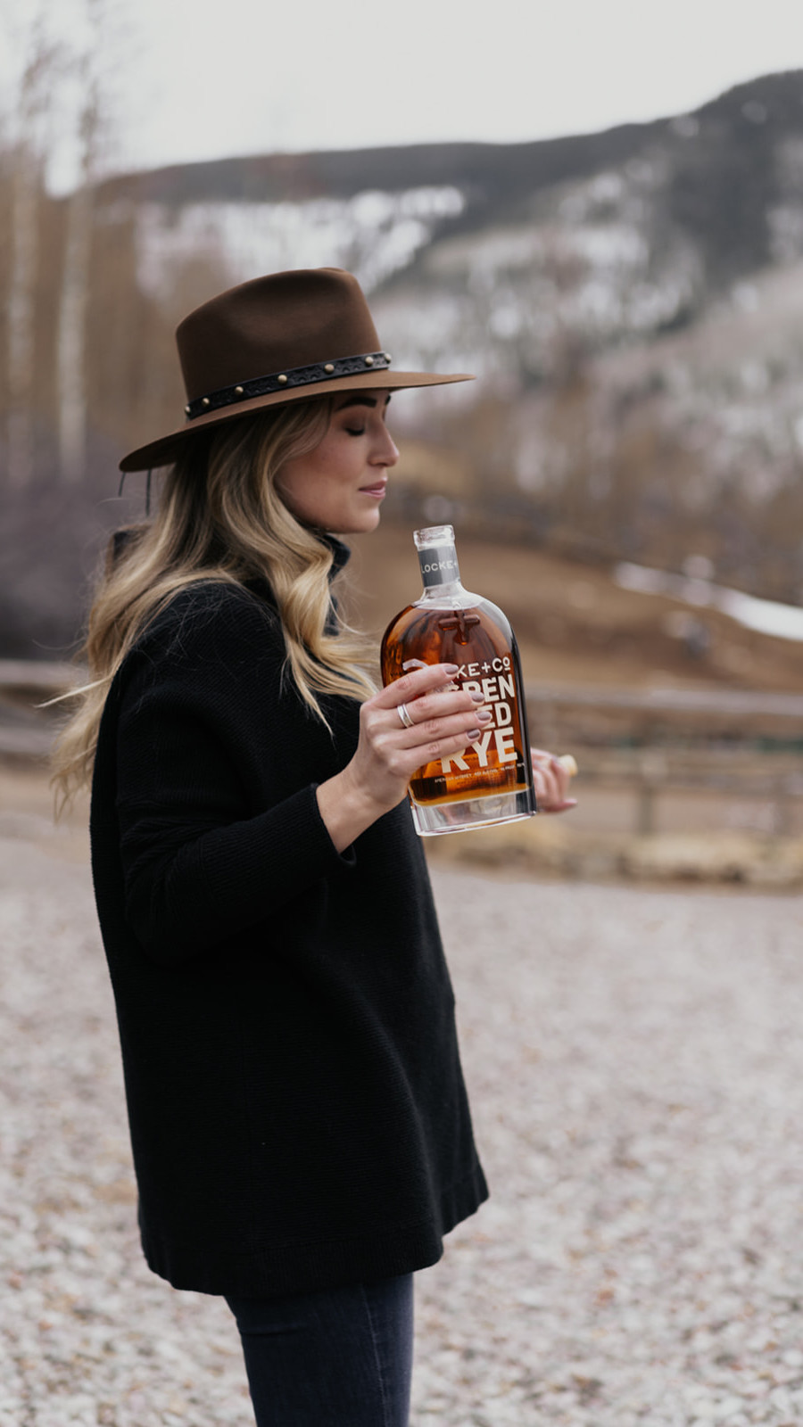 Women holding an open bottle of Locke + Co. Aspen Aged Rye Whiskey Bottle on a winter scene ranch