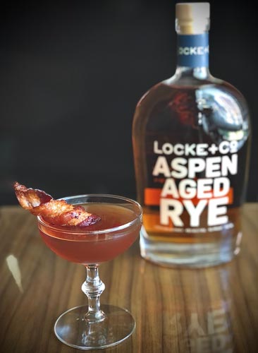 Maple Bacon Manhattan and Locke + Co. Aspen Aged Rye Whiskey Bottle on a wood table