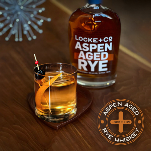 Locke + Co Old Fashioned on a wood table next to a bottle of Locke + Co Aspen Aged Rye Whiskey