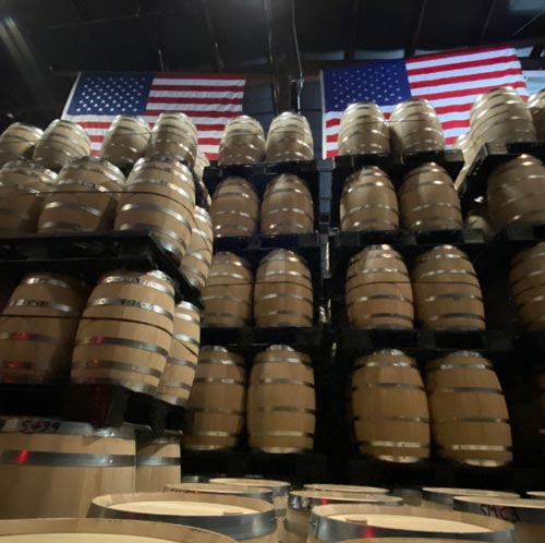 Locke + Co Aspen Aged Rye Whiskey Barrels Aging and Two American Flags hanging from the ceiling