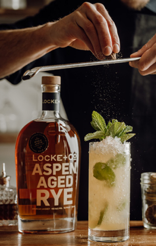 Aspen Swizzle Cocktail with freshly grated nutmeg and a Locke + Co-Aspen Aged Rye Whiskey Bottle