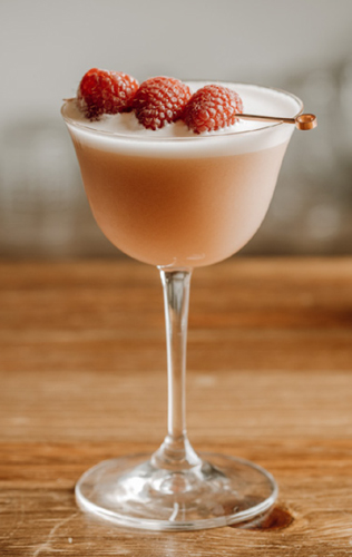 locke+club cocktail with three raspberries on pick laid over top of glass