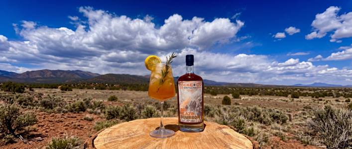 Firebreak Spritz cocktail and Locke + Co Distilling Big Blaze Bourbon bottle with mountain landscape in background